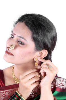 A beautiful Indian woman wearing jewelery while getting ready in her traditional attire for a ceremony.