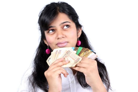 A metaphorical portrait of an Indian teenage girl holding cash and credit cards, on white studio background.