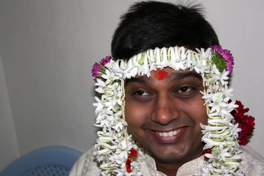 A portrait of a jovial Indian groom in traditional attire of flowers and garlands.