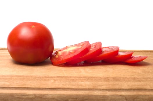 Whole and sliced tomatoes on a cutting board isolated on a white background.