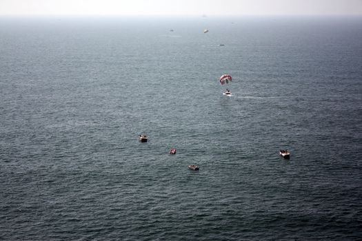 Tourists enjoying different boats, speedboats and parasails in the ocean waters.