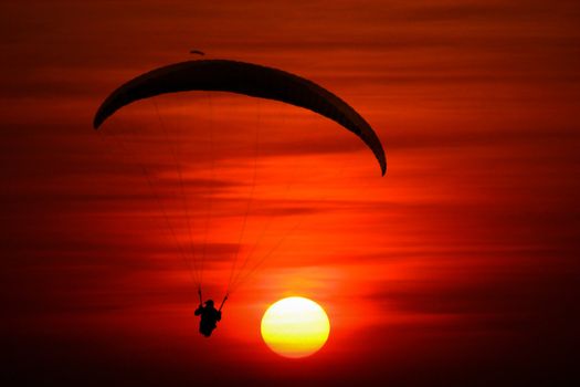 A beautiful background with a silhouette of a paraglider, in front of a setting sun.
