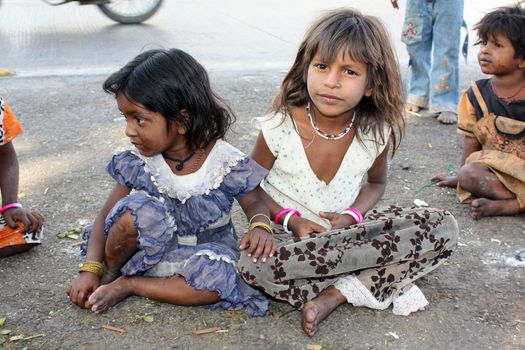 Poor beggar children in India sitting and playing on the side of a street.