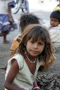 A portrait of an inquisitive beggar girl from India, sitting on the street-side.