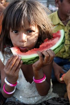 A poor Indian beggar girl hungrily eating a watermelon.