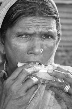 A black & white portrait of a poor old Indian woman eating watermelon. Focus is on the hand and melon.