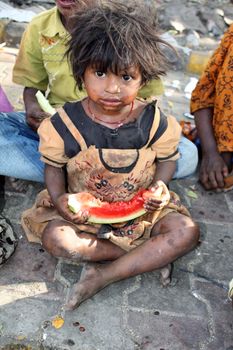 A poor beggar girl from India eating a watermelon.