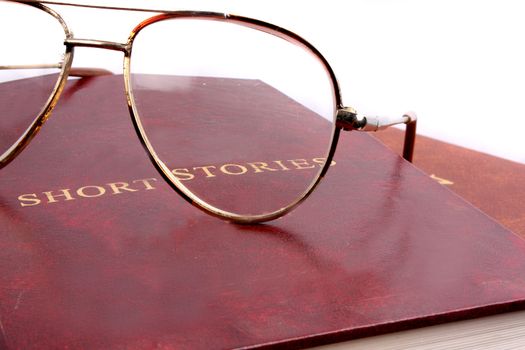A leather cover book of short stories & reading glasses with metallic frame on them.
