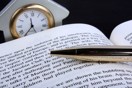 A metaphorical image of a clock, closed ball point pen and a book, depicting the objects left by a person during break time.