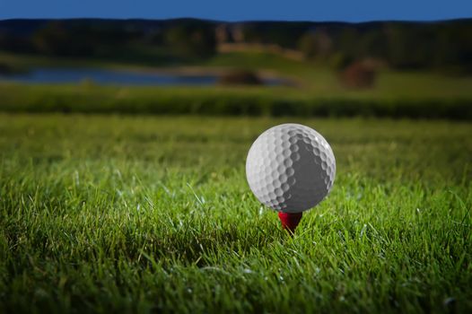 Image of a beautifully lit golf ball on a red tee with course in background
