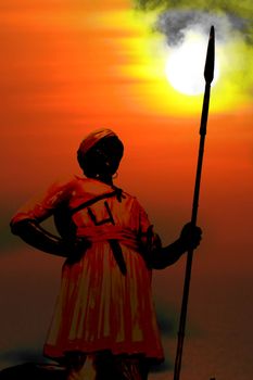 The silhouette of an ancient statue of an Indian warrior with a spear on sunset. The clouds and the darkness have been created for war effect.