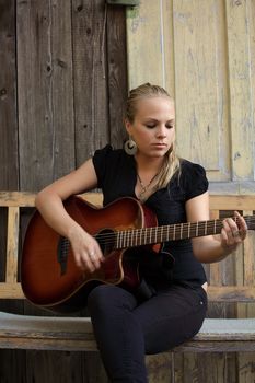 Photo of a beautiful blond female playing her acoustic guitar on an old wooden bench.  