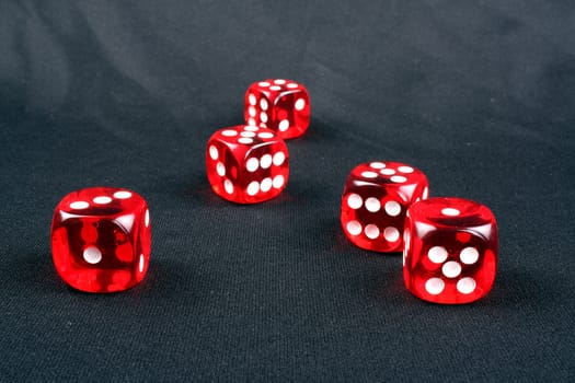 A set of five red dices on a black fabric.