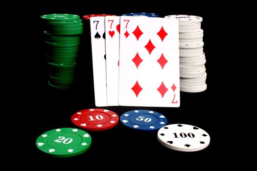 A poker winning hand called 'Three of a Kind' (consisting of three similar cards - sevens in this example) leaning on a stack of gambling chips, isolated on black studio background.