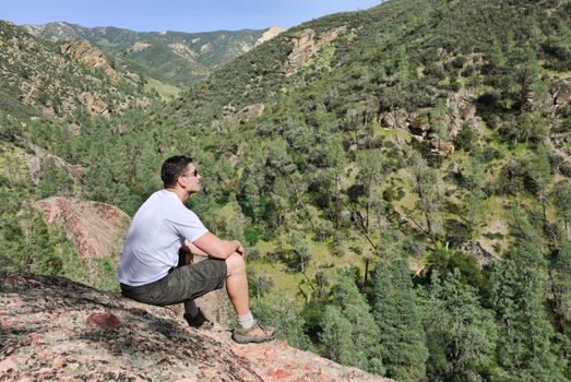 Handsome young man sitting on the rock enjoying the view.