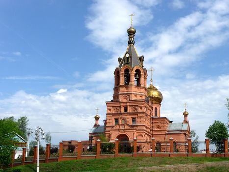 Red urban church on a background of blue sky with clouds