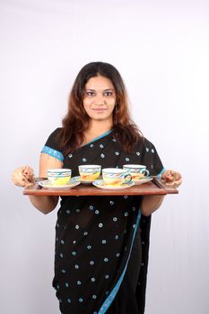 A traditional young Indian woman getting tea in a wooden serving tray.
