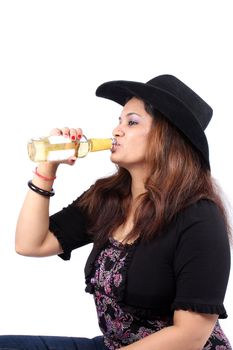 A young Indian woman in hat drinking a orange alcoholic beverage, on white studio background.