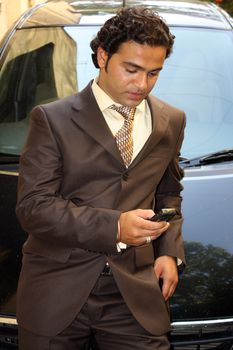 A young Indian businessman leaning on his cars checking the missed calls on his cellphone.