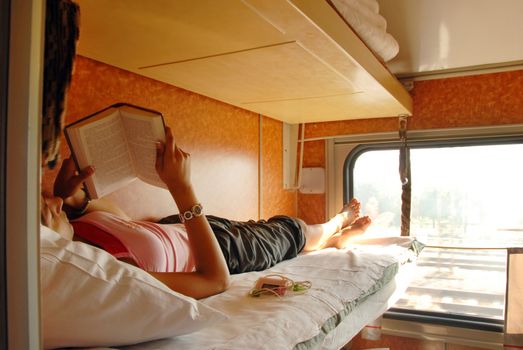 girl lying and reeding a book in sleeping wagon in train