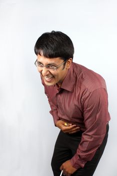 A young Indian man laughing heartily over a joke, holding his belly.