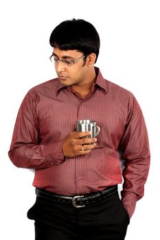 A tensed Indian guy/executive holding a coffee cup, leaning against a white wall.