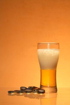 Bottle caps lying near glass of light beer with foam