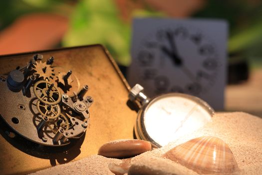 Abstract background with old clock mechanism standing on sand with stones and shells