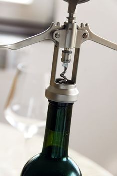 silver metallic cork screw opening a green wine bottle