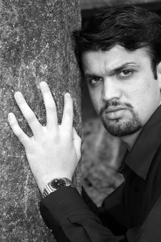 A black & white portrait of a handsome Indian guy near a tree.
