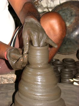 A closeup view of a potter shaping his pot on the rotating wheel.