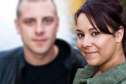 A young happy couple standing by a lake in autumn.  Shallow depth of field with focus on the woman.