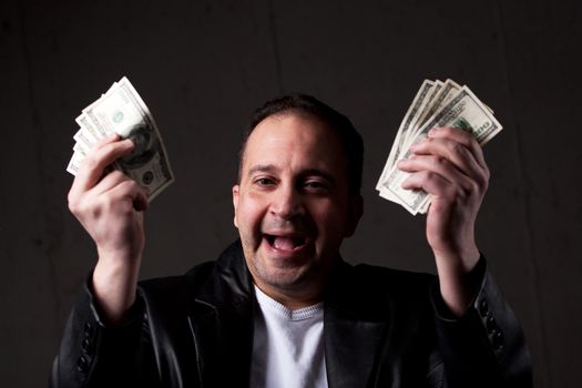 A man celebrating holding handfuls of green American cash money. Shallow depth of field with focus on the face.