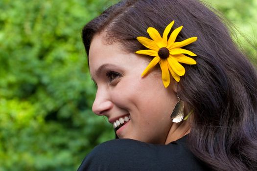 A happy and beautiful young brunette woman wearing a black eyed susan wildflower in her hair.