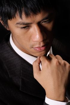 Thinking expression of oriental young business man, closeup portrait in dark background.
