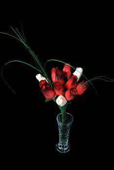 A bouquet of wooden roses in a glass vase, isolated against a black background