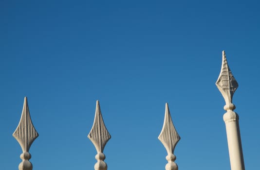 Four iron spears on top of a fence with blue sky background