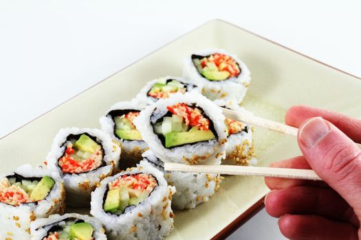 A hand holding a set of chop sticks with sushi.