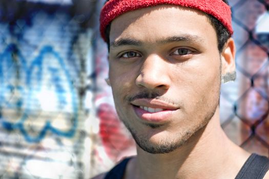 A basketball player posing at the park outdoors in front of a chain linked fence and some grafitti.