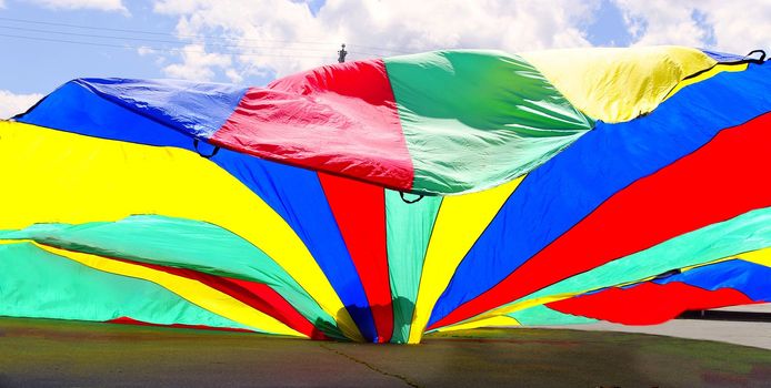 lone shadowy silhouette toddler crawling inside  technicolor parachute  breezy summer day carefree .contrast of tiny and gigantic
