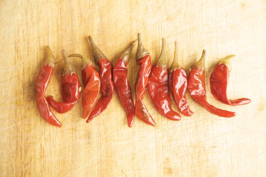 Red Hot Chillies on a wooden kitchen table, lit with a large light source from the right.