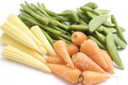 Fresh Baby Carrots, Baby Corn, Long Green Beans and Sugar Snaps, isolated on a white background table, lit with a large light source from the above right.