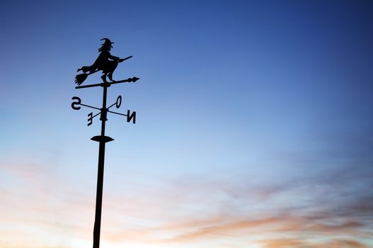 A silhouette of a weather vane with a witch on top. 