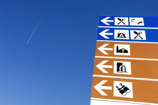 A picture of some blue and white directional signs with icons printed on them, indicating places of interest to tourists.