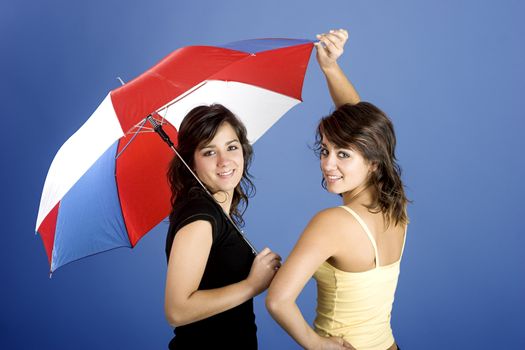 Beautiful young twins posing with an umbrella on a blue background