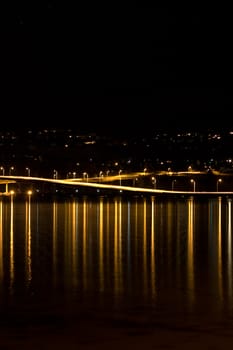 a vertical night photo of a bridge lights water reflections