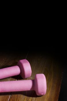 Two pink dumbbells laying on a wooden surface.