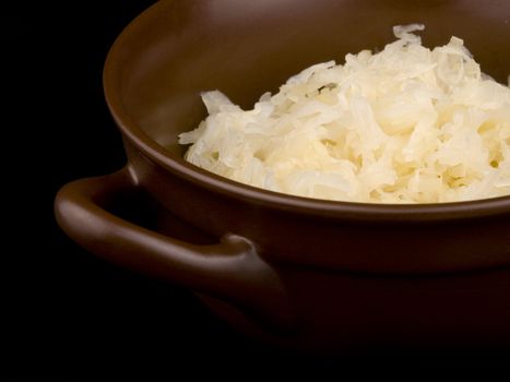 Ceramic bowl filled with sour cabbage on black background