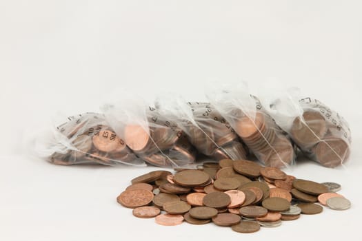 A pile of loose coins with bags of coins in the background isolated on white.