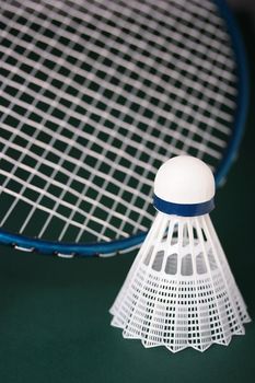 A white synthetic shuttlecock and a blue badminton racquet on a green background.